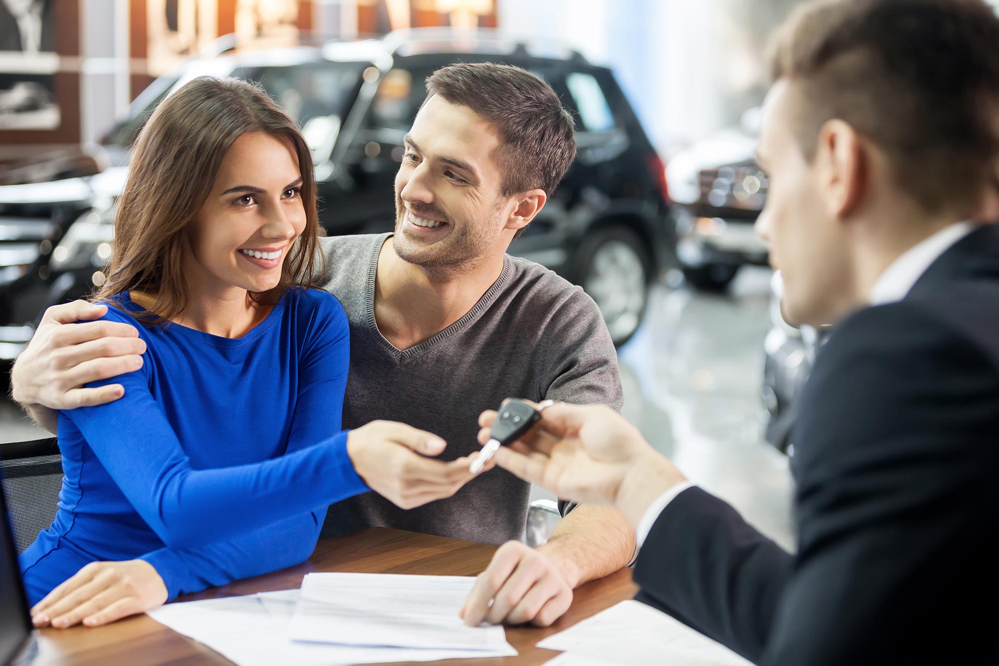 Photo of couple receiving vehicle keys from salesperson in a car dealership